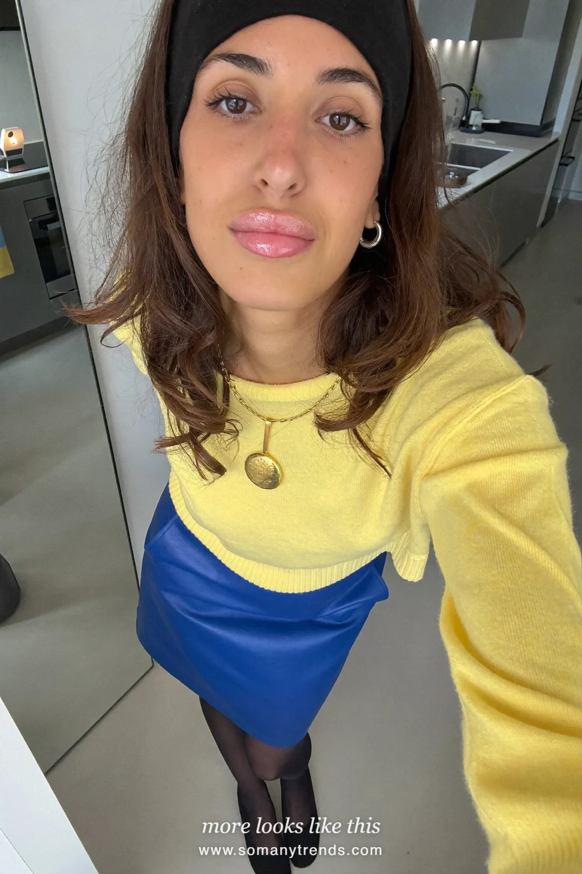 Woman in a lemon yellow knit sweater, cobalt blue leather midi skirt, black opaque tights, black pumps and a long black coat, outfit 15