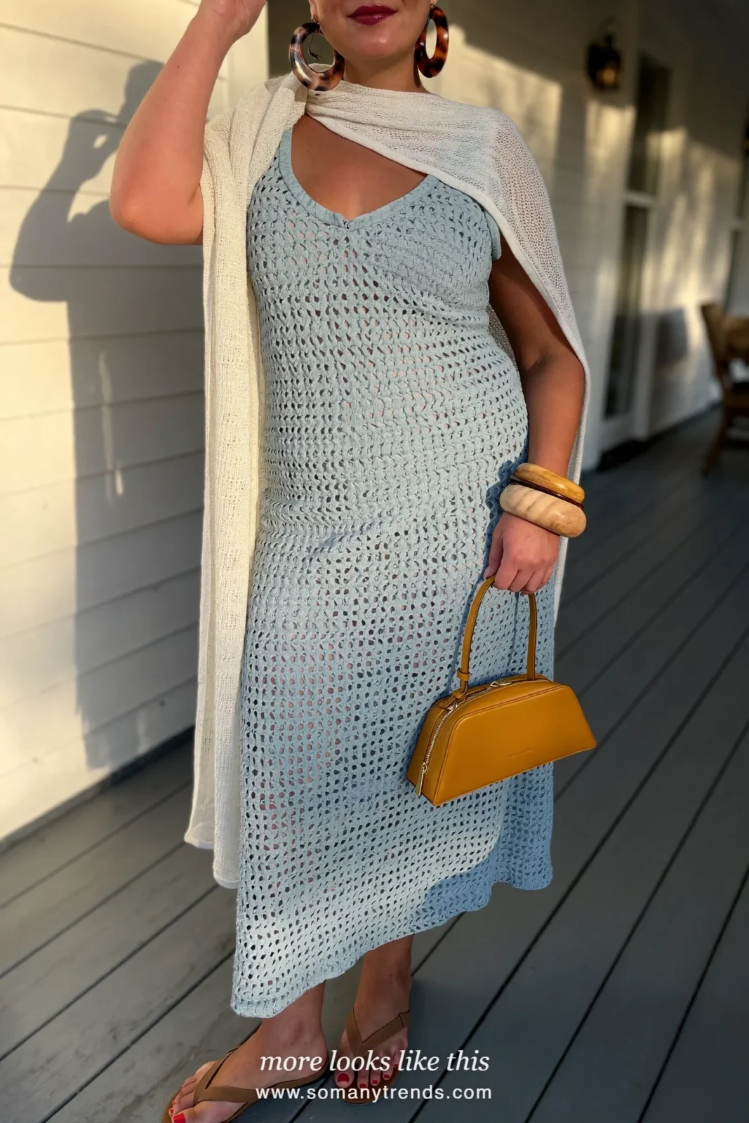 Woman in a pale blue crochet maxi dress, small mustard box bag and flat sandals on a white porch at golden hour, outfit 16