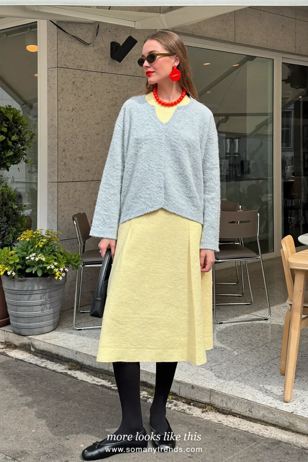 Woman in a butter yellow long-sleeve midi dress, baby blue cardigan over the shoulders, sheer black tights and black ballet flats outside a café, outfit 17