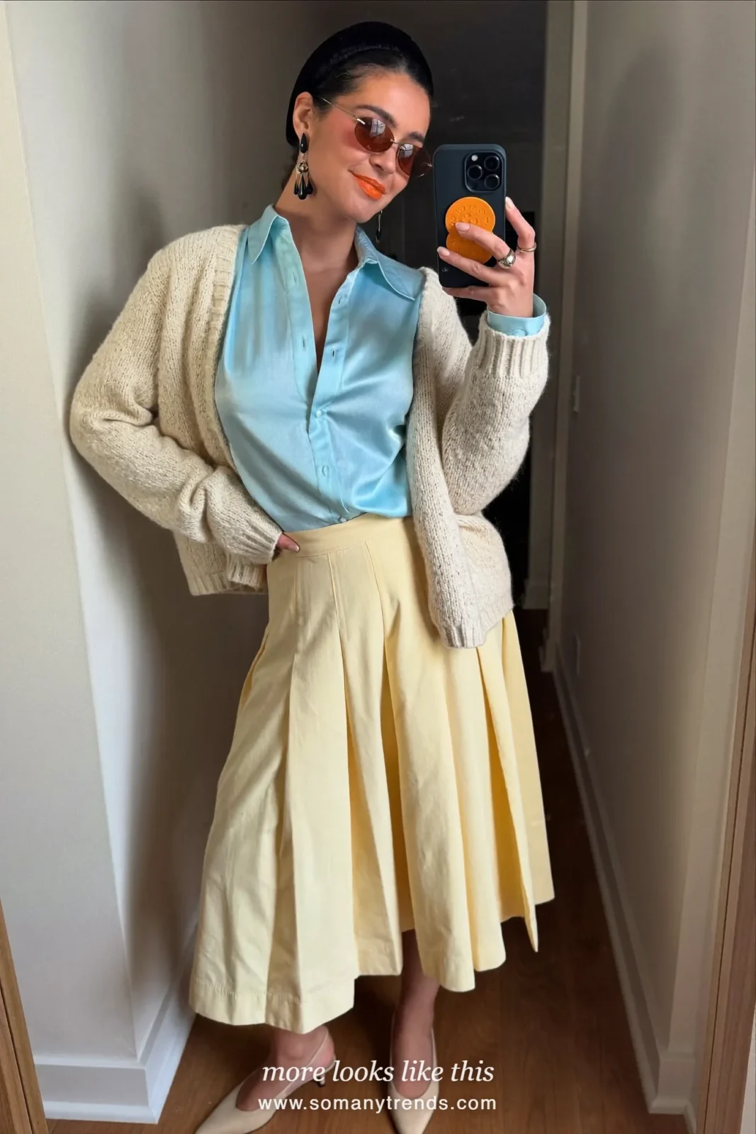 Woman in a pale blue satin blouse, butter yellow pleated midi skirt, cream cardigan and slingback pumps at a café terrace, outfit 21