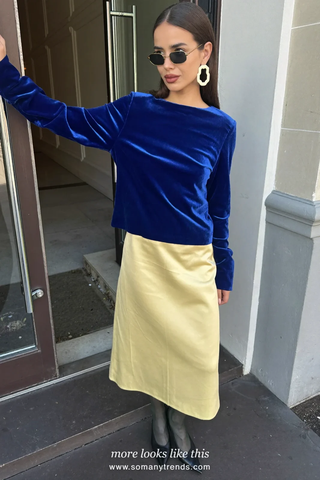 Woman in a cobalt blue velvet long-sleeve top, lemon yellow satin midi skirt, sheer black tights and black pumps at a holiday party venue, outfit 23