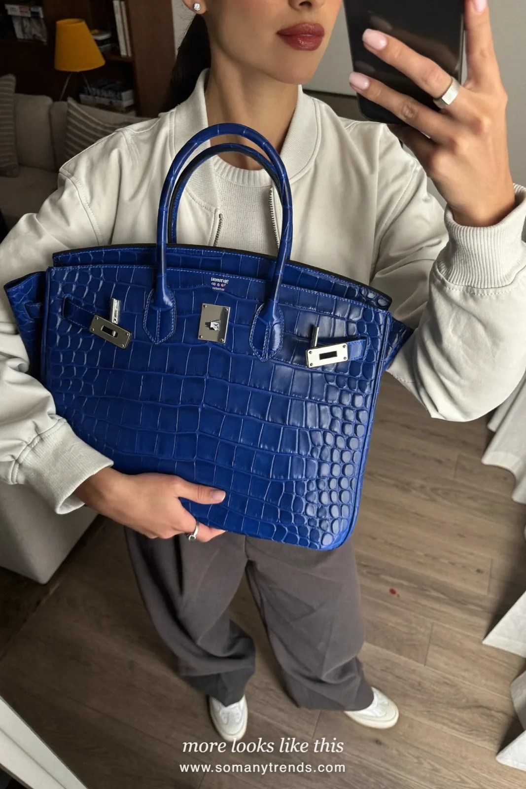 Woman in a white bomber jacket, gray pants, white sneakers and an oversized cobalt blue croc tote bag, outfit 12