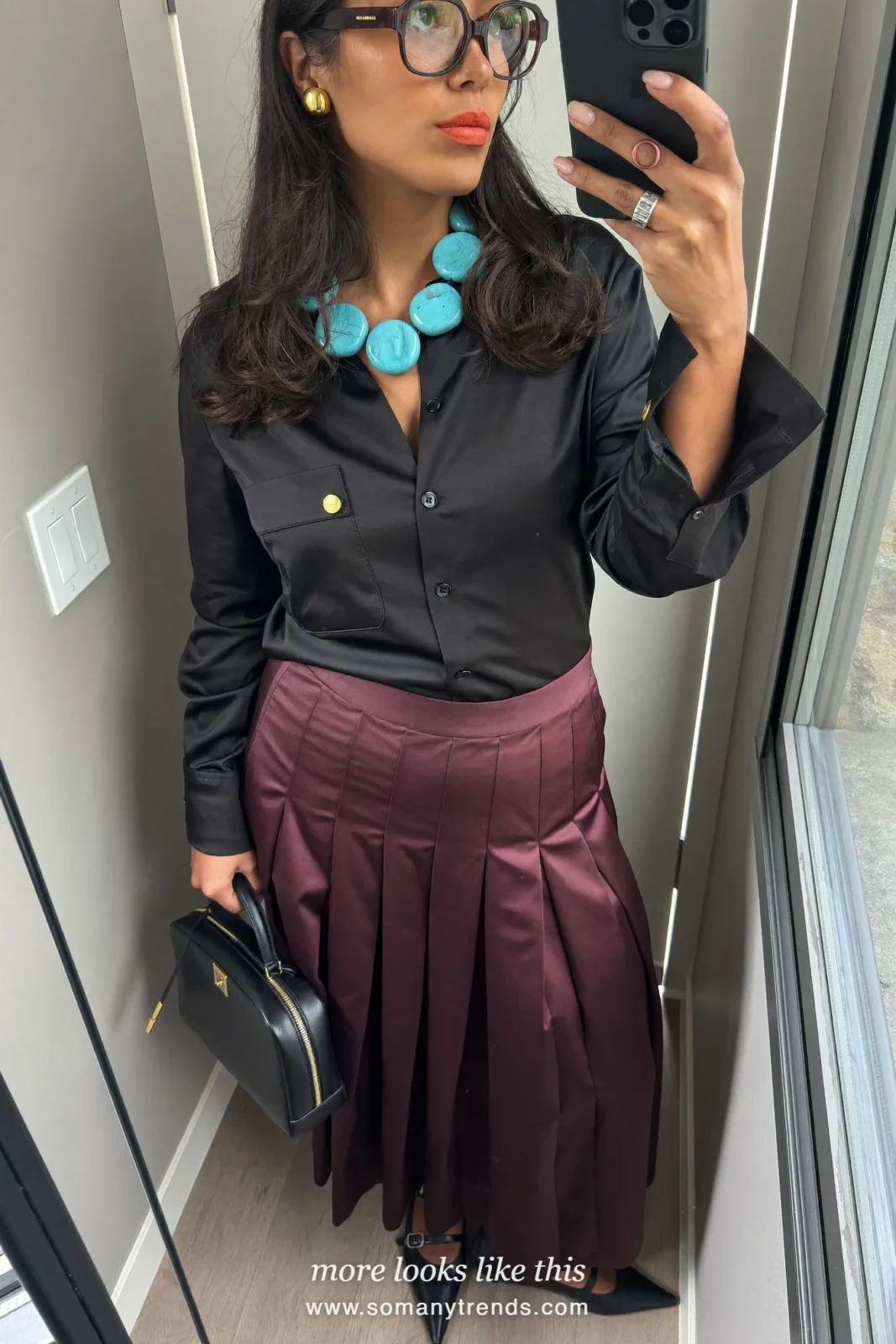 Woman in a black satin blouse, deep burgundy pleated midi skirt and black pointed flats, outfit 12
