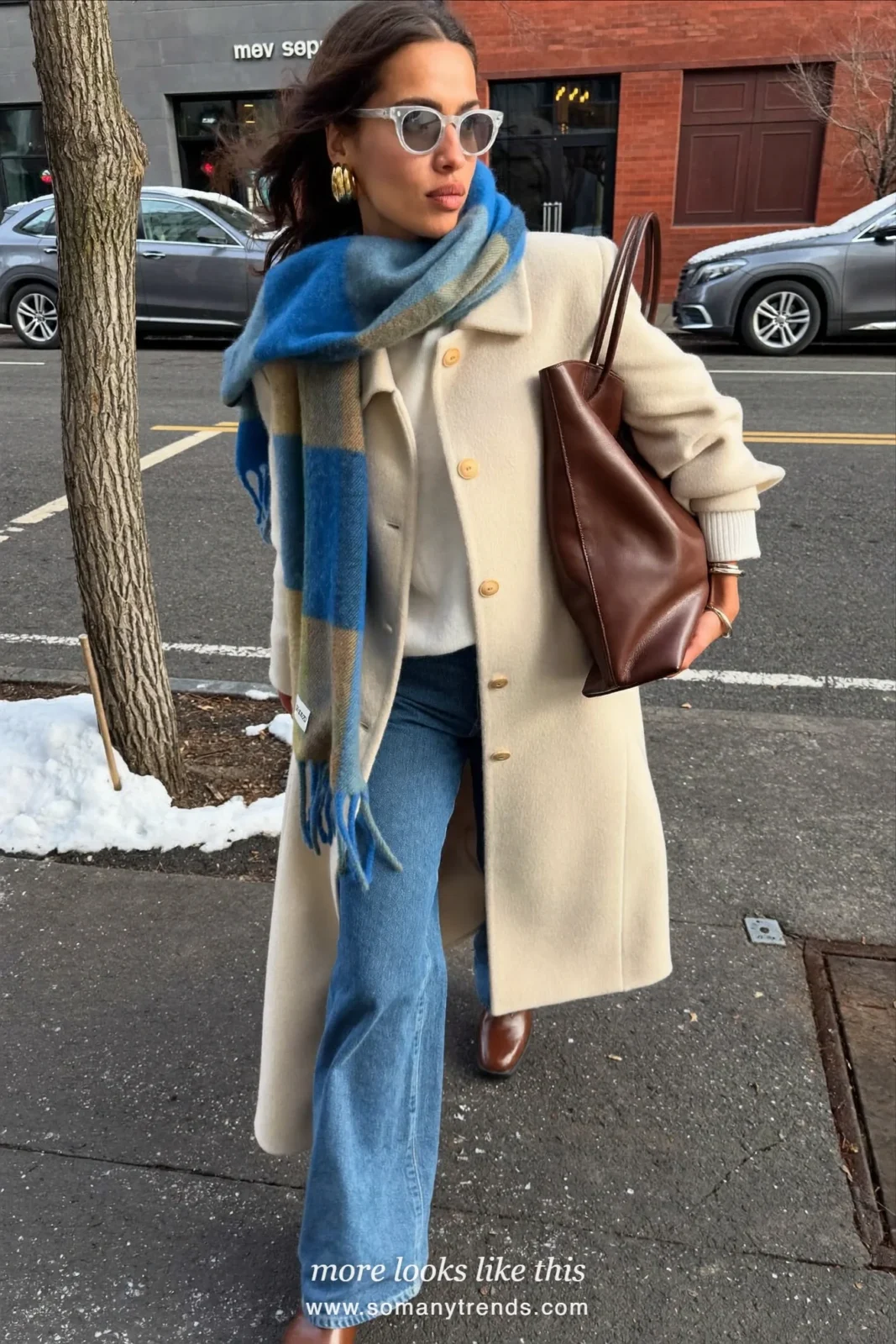 Woman in a butter cream long wool coat with a blue plaid wool scarf, white knit sweater, blue jeans and brown leather boots on a snowy New York street, outfit 1
