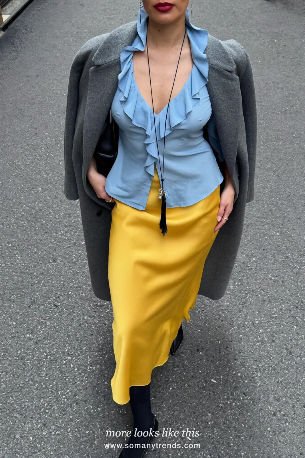 Woman in a powder blue ruffle blouse, golden mustard satin slip skirt, black opaque tights, black pointed pumps and a long gray coat, outfit 8