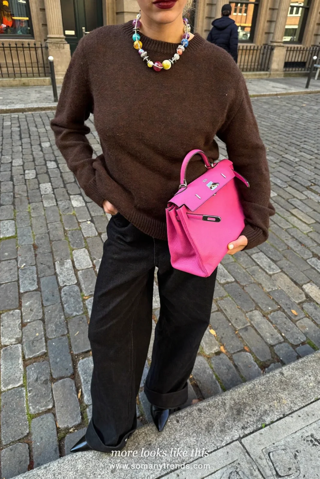 Woman in a chocolate brown chunky knit sweater, black straight jeans, black ankle boots and a fuchsia pink bag, look 1