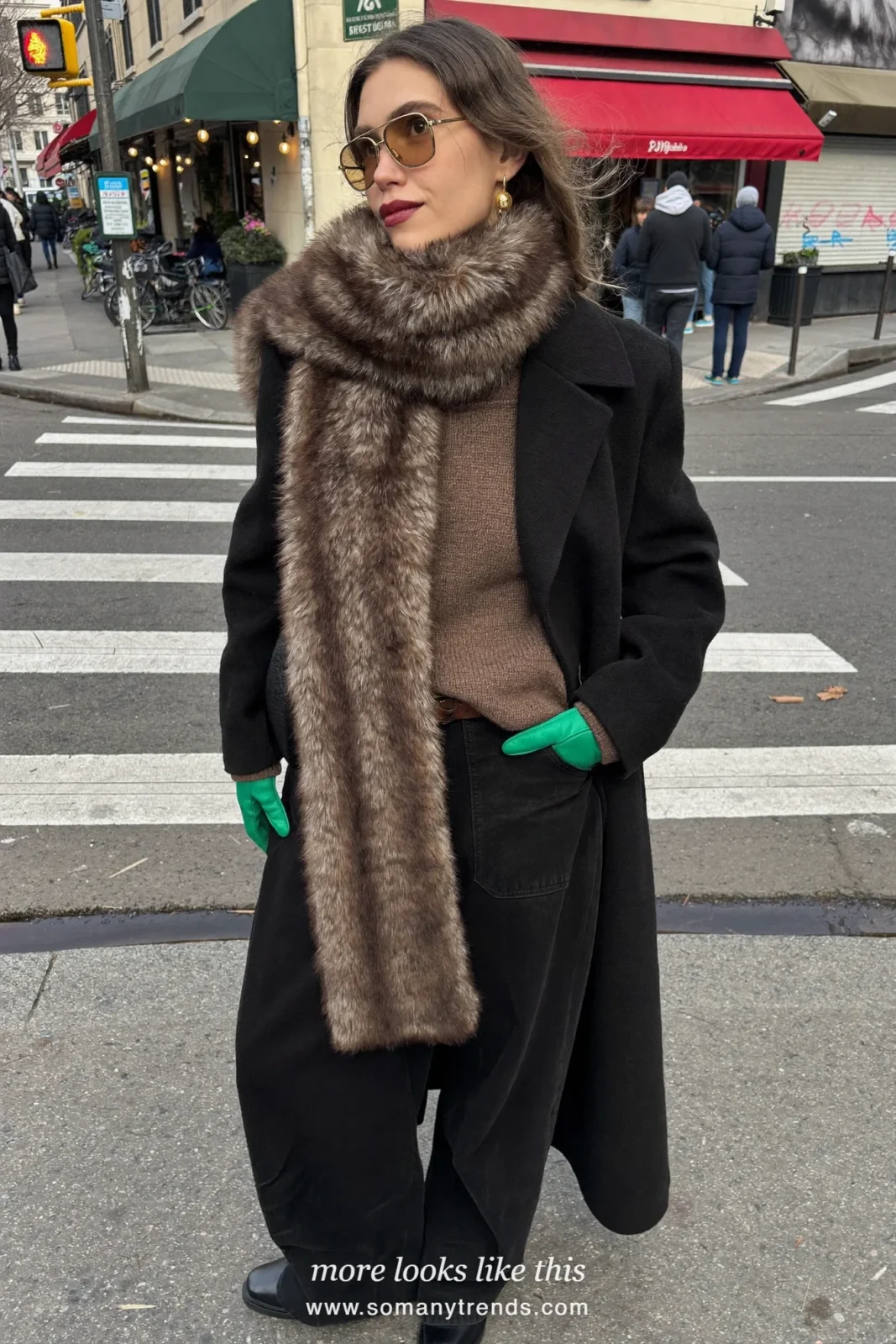 Woman in a long black wool coat with a brown faux-fur scarf, chocolate knit, black pants and emerald green gloves, look 10