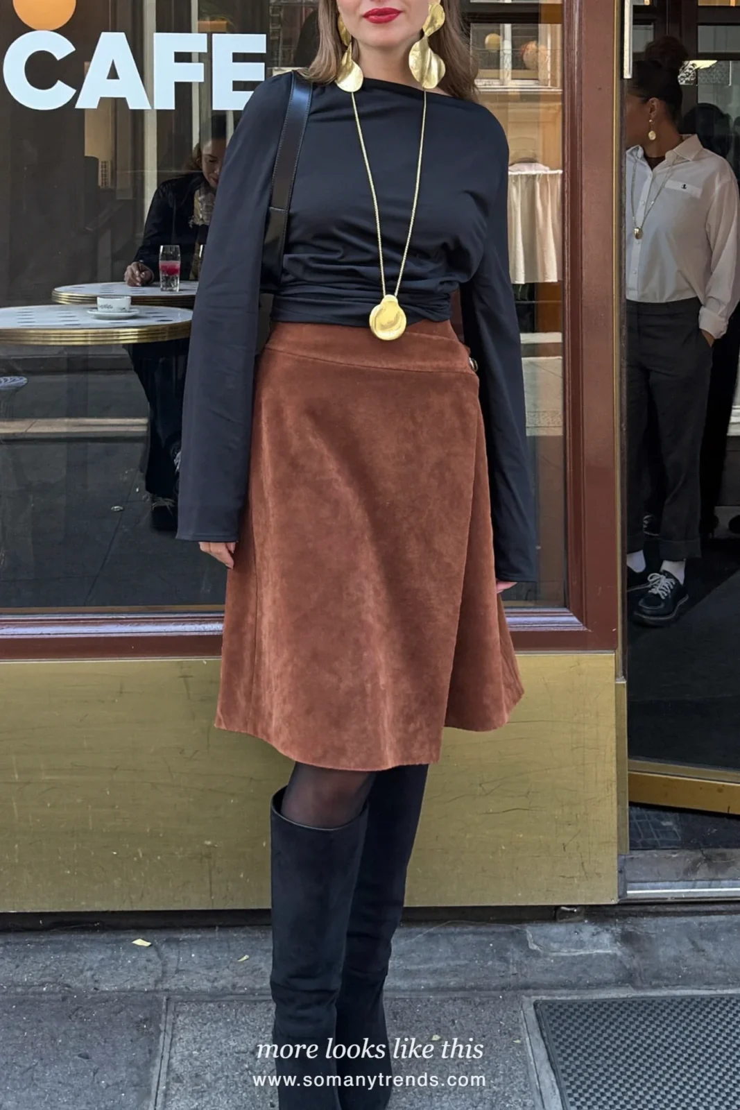 Woman in a black wrap top, rust brown suede midi skirt, black knee boots and a butter yellow bag, look 16