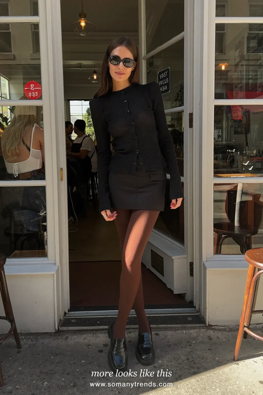 Woman in a black mini skirt, black knit top, chocolate brown opaque tights, black chunky loafers and a fuchsia bag, look 19