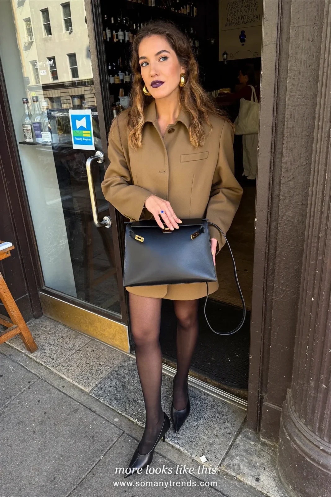 Woman in a camel blazer dress, sheer black tights, black pointed pumps and a black bag, look 23