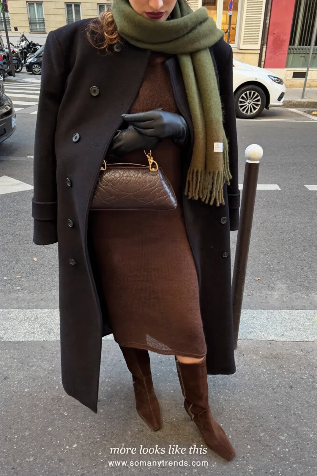 Woman in a long black wool coat over a chocolate brown knit midi dress with brown suede knee boots and an olive green scarf, look 28