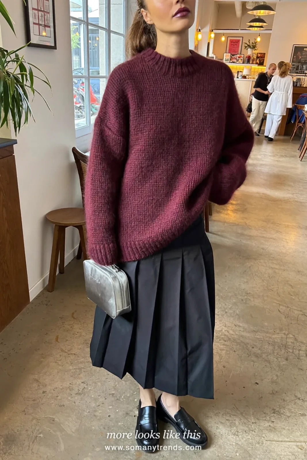 Woman in a burgundy chunky sweater, black pleated midi skirt, black loafers and a silver bag, outfit 28