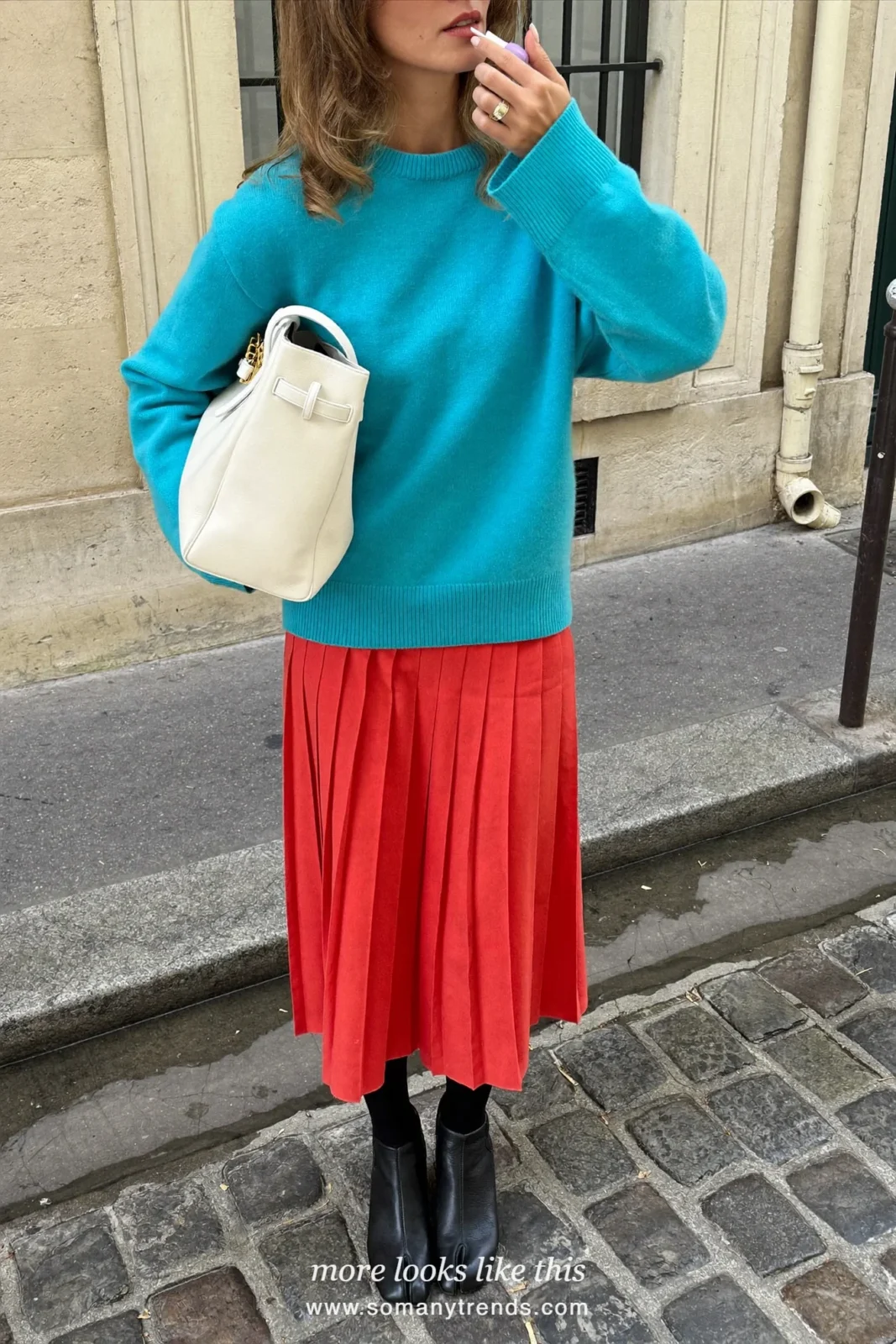 Woman in a saturated aqua knit sweater, coral red pleated midi skirt, black tights and black ankle boots, outfit 1