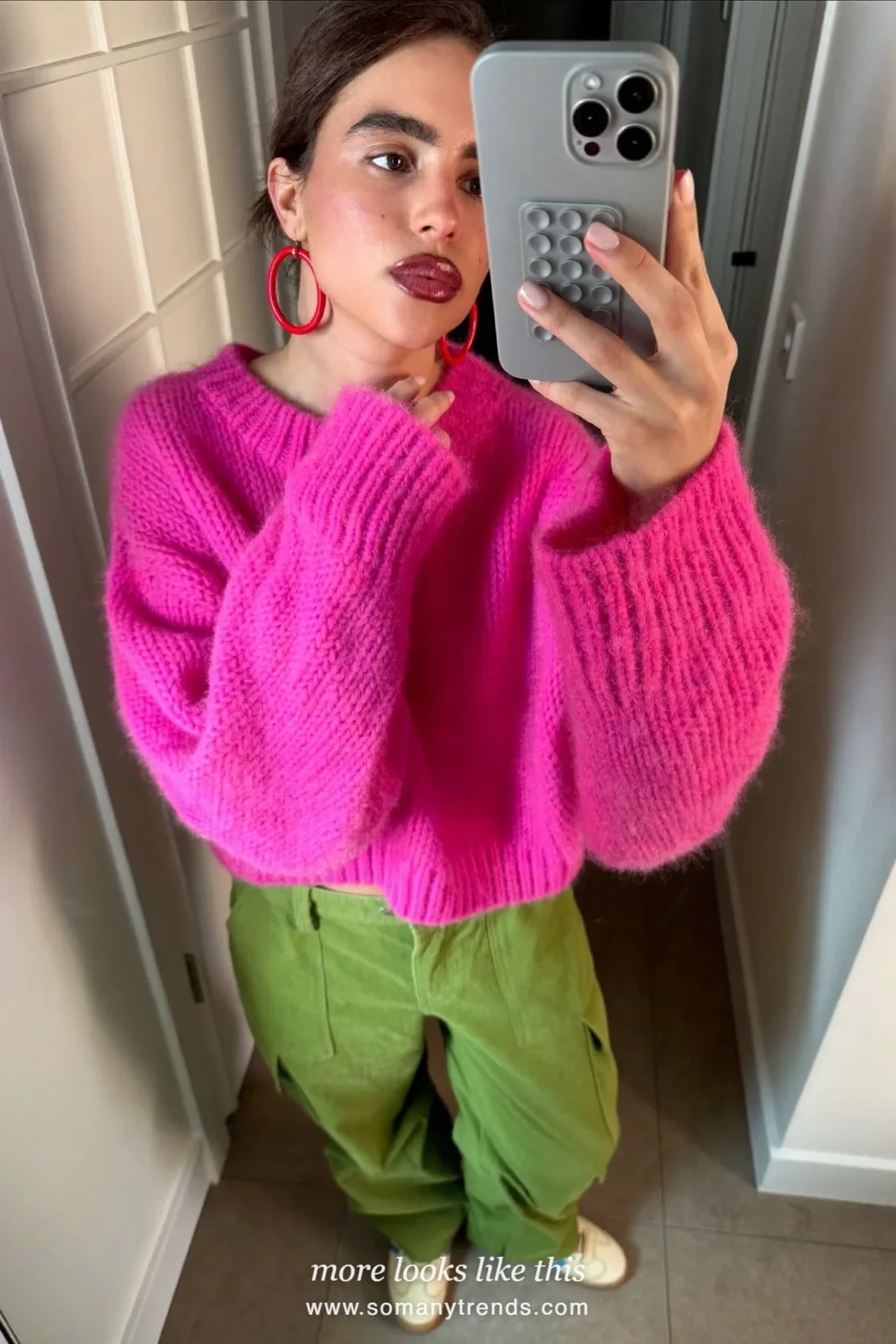 Woman in a bright pink chunky sweater, vivid moss green cargo pants and cream low sneakers, mirror selfie in a hallway, outfit 3