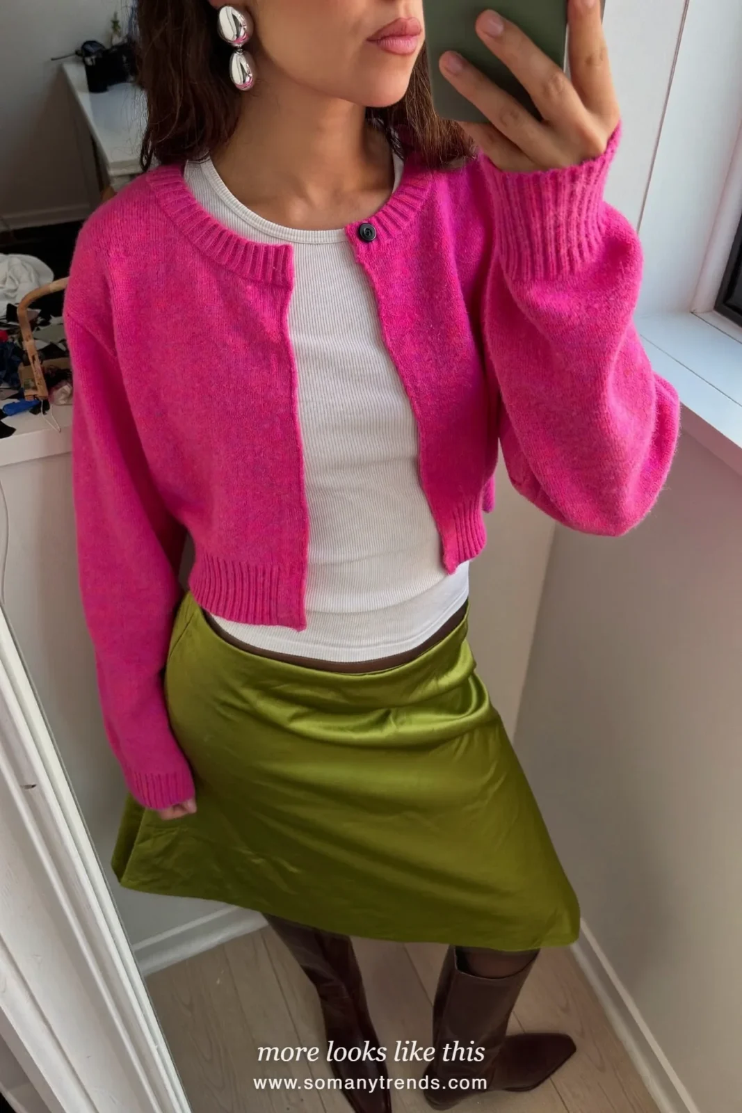 Woman in a bright pink cardigan, white ribbed top, moss green satin midi skirt and brown knee-high boots, mirror selfie in a dressing room, outfit 6