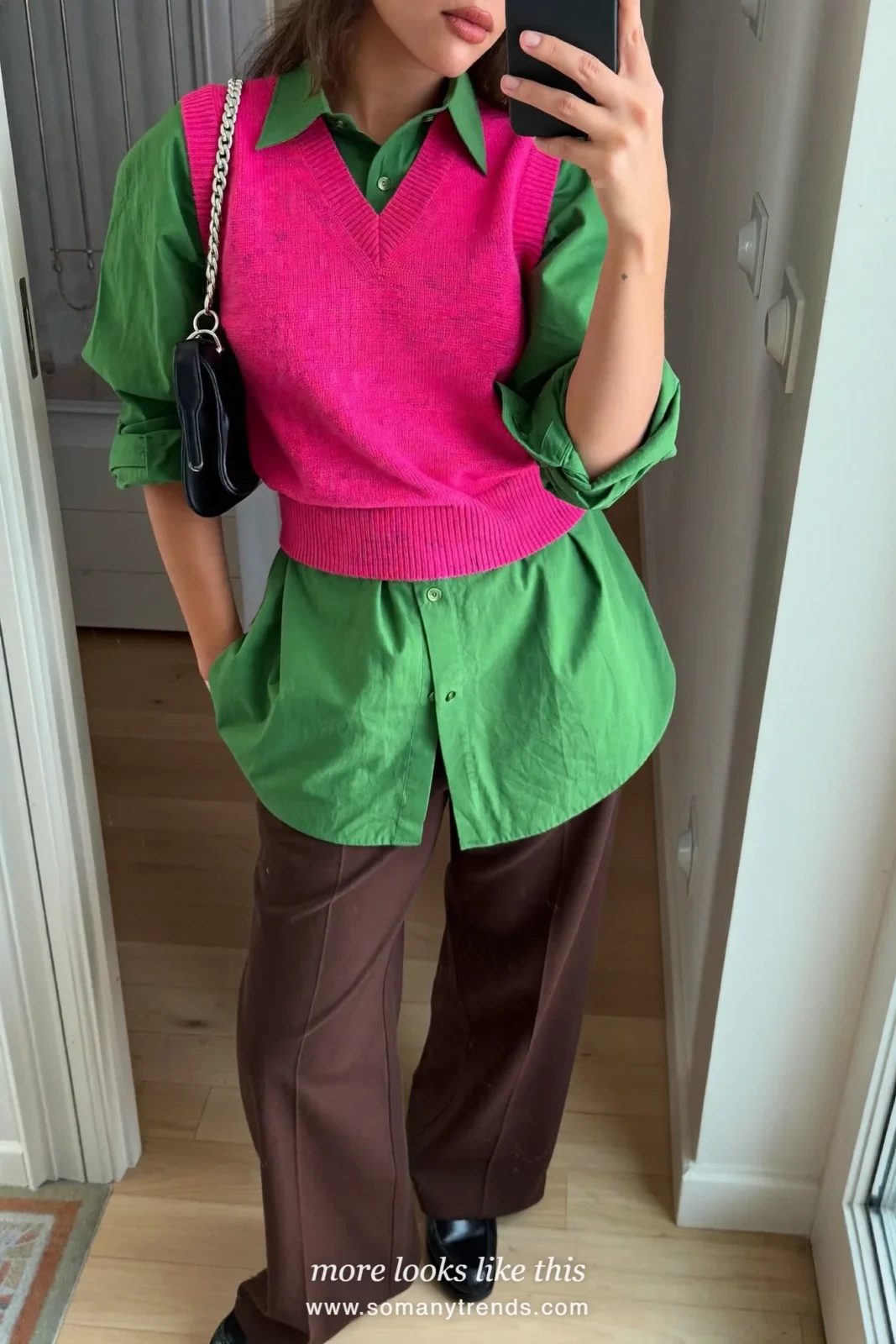 Woman in a bright pink knit vest, olive green shirt, brown wide-leg pants and loafers, mirror selfie in an entryway, outfit 10