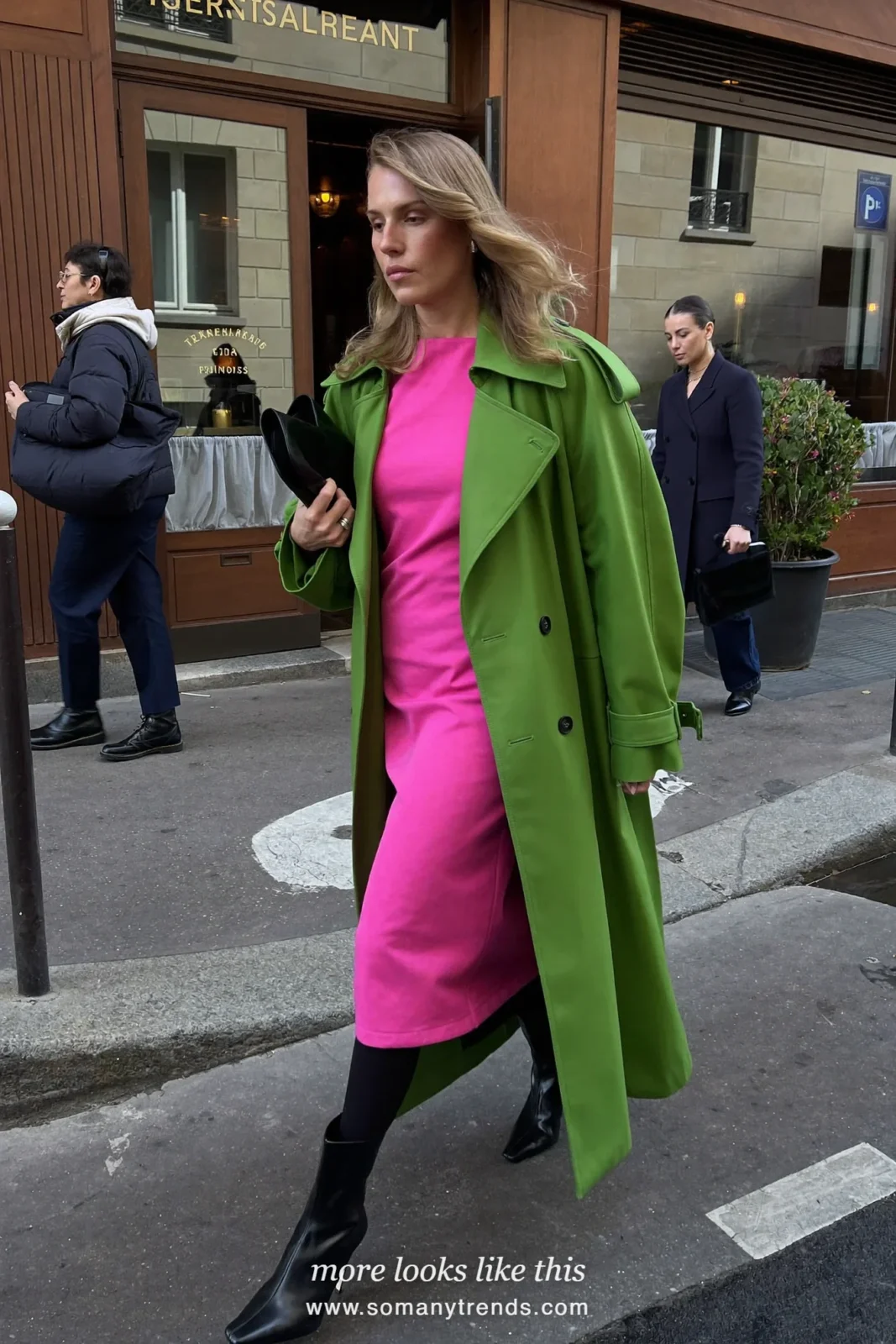 Woman in a moss green trench coat open over a bright pink midi dress with black tights and ankle boots, outfit 11