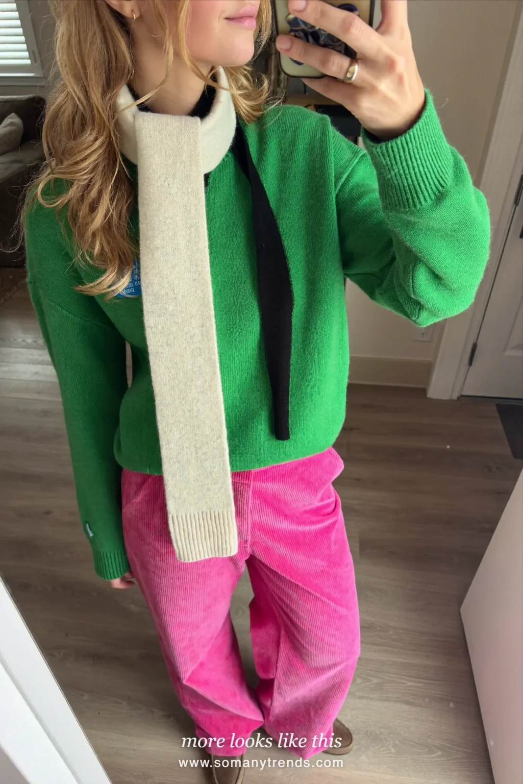 Woman in a moss green knit sweater, bright pink wide-leg corduroy pants, brown suede loafers and a cream scarf, outfit 12