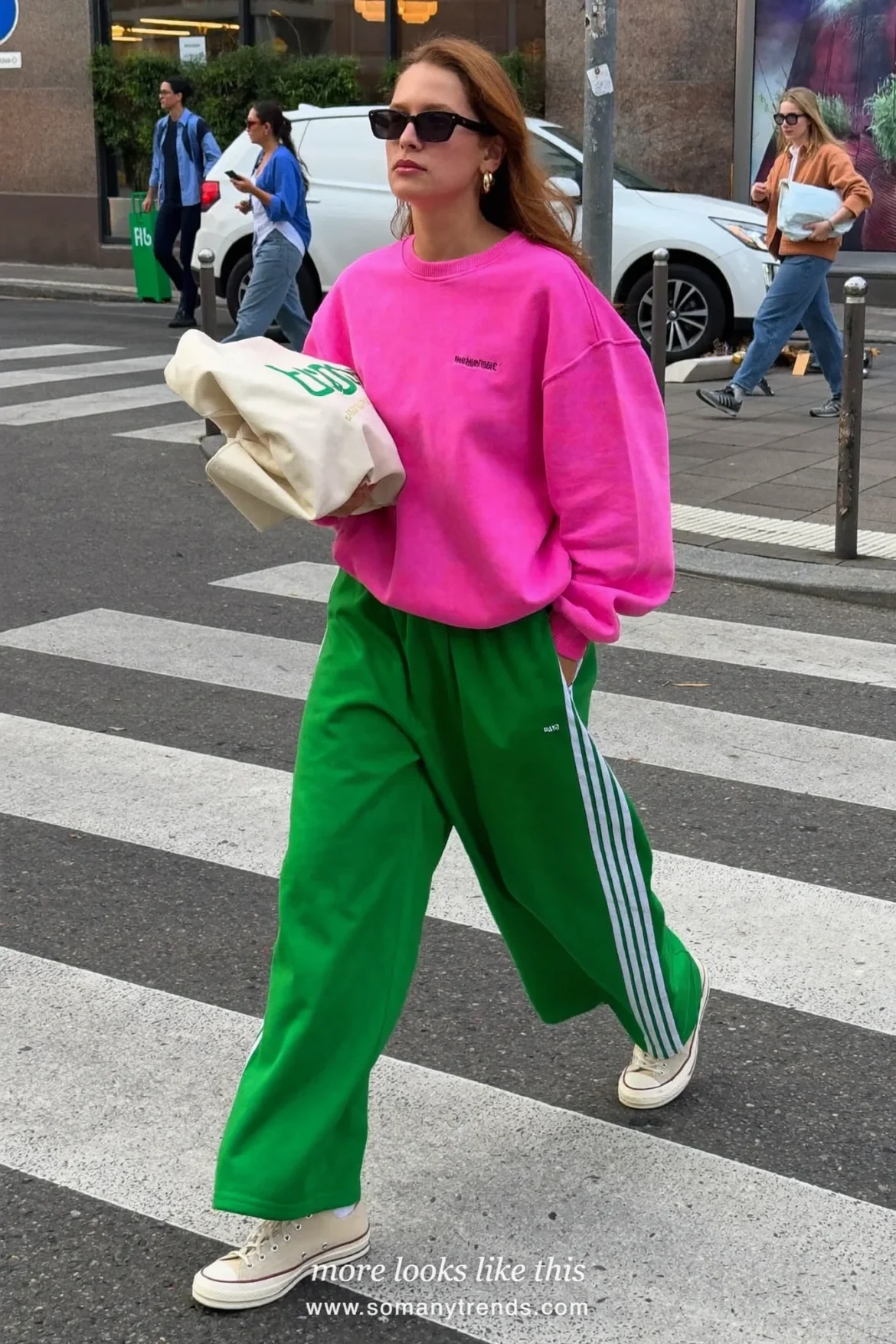 Woman in a bright pink sweatshirt, moss green track pants with side stripes and cream sneakers, outfit 14