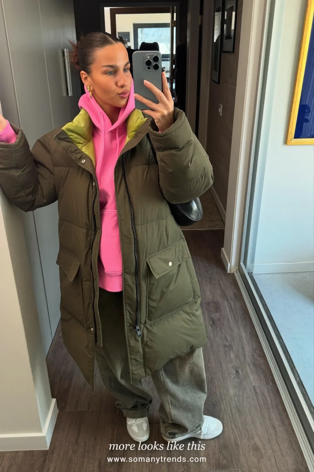 Woman in a long moss green parka, bright pink hoodie, gray wide jeans and sneakers, outfit 18