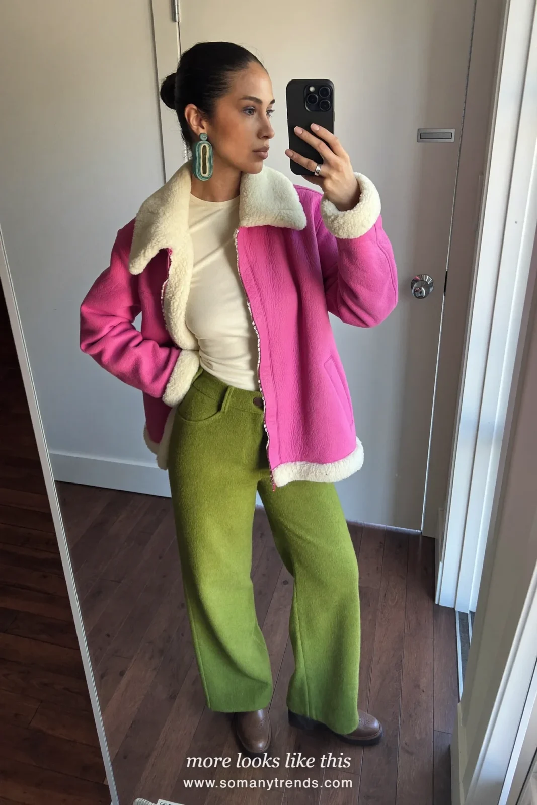 Woman in a bright pink shearling jacket, cream knit top, moss green pants and brown boots, outfit 24